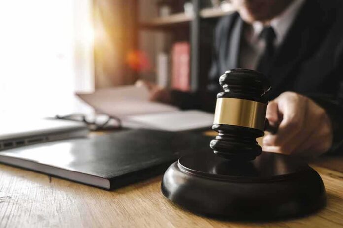 shutterstock_1061028056 Judge's gavel on desk with person reading documents in background