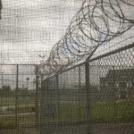 1,250 Men Next Door? Tiny Village Erupts Barbed wire on chain-link fence at a prison yard