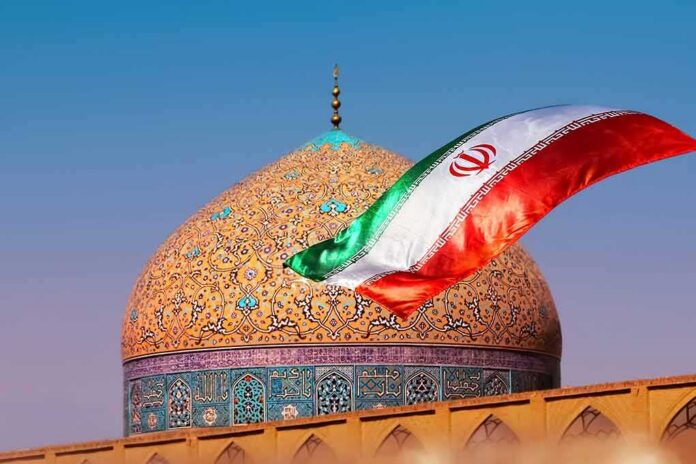 Iranian flag waves before an ornate mosque dome at sunset