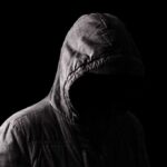 Hooded figure in shadow on black background