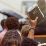 Protestant Database Drops — Cover-Up Claims Rattle Leaders Hand holding a Bible in a crowded church service