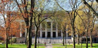 Students walking on a university campus with autumn trees and a historic building in the background