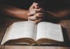 Hands clasped over an open book on a wooden table