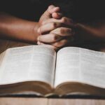 Judge Slaps Down Faith Enforcers Hands clasped over an open book on a wooden table