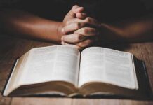 Judge Slaps Down Faith Enforcers Hands clasped over an open book on a wooden table