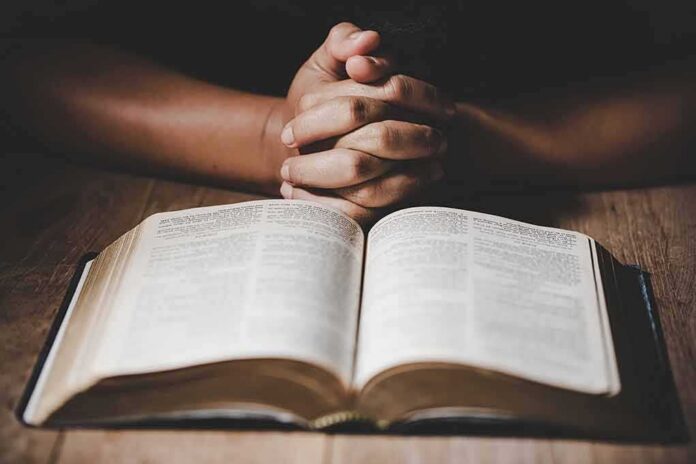 shutterstock_1429250558 Hands clasped over an open book on a wooden table
