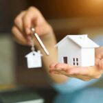 Decades-Long Deals Trap Military Families Hands holding a house model and a key with house-shaped keychain