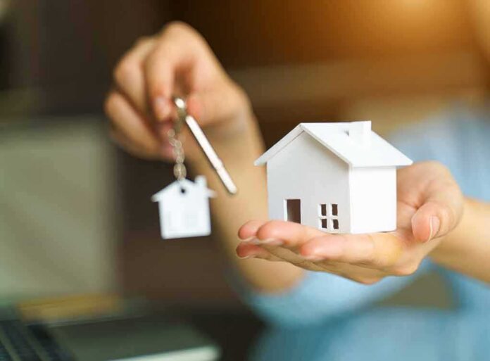 shutterstock_1716324079 Hands holding a house model and a key with house-shaped keychain
