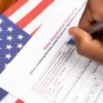 Hand filling out a voter registration form beside an American flag