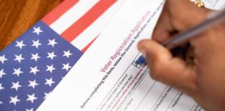 Hand filling out a voter registration form beside an American flag