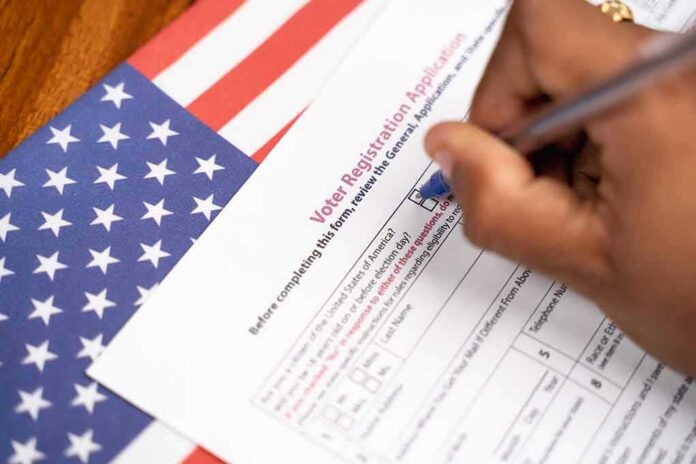 shutterstock_1762483943 Hand filling out a voter registration form beside an American flag