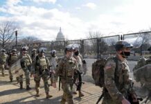 Soldiers in riot gear patrol near a fenced government building