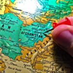Hand placing a red pushpin on Afghanistan on a map