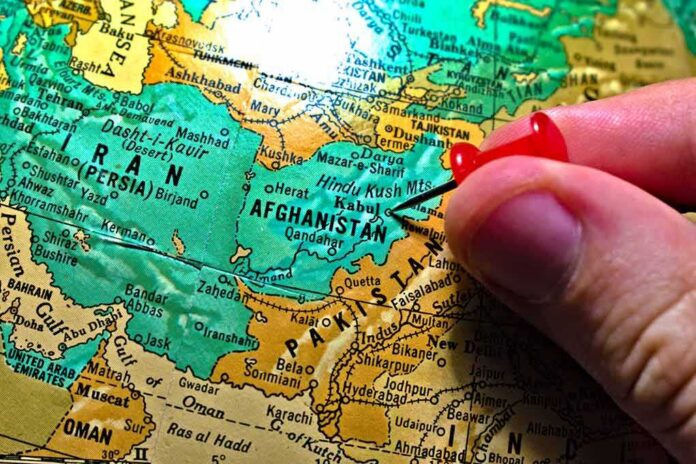 Hand placing a red pushpin on Afghanistan on a map