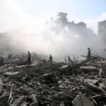 UN Warns: Gaza Hunger Still Raging — Where Did Aid Go? People walking through smoke-filled urban rubble