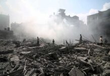 UN Warns: Gaza Hunger Still Raging — Where Did Aid Go? People walking through smoke-filled urban rubble