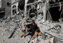 Man with two children sitting amid rubble of a destroyed building