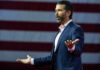 Donald Trump Jr. speaking on stage with arms outstretched