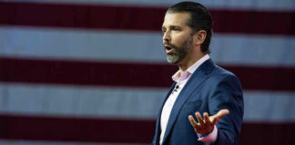 Donald Trump Jr. speaking on stage with arms outstretched