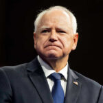 Whistleblowers Crushed – Retaliation Claims Rock Minnesota Tim Walz in a dark suit and tie at an event