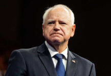 Whistleblowers Crushed – Retaliation Claims Rock Minnesota Tim Walz in a dark suit and tie at an event