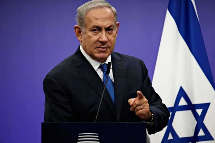 man in suit speaking at a podium with an Israeli flag