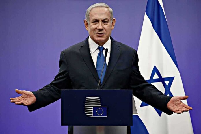 man in suit speaking at a podium with Israeli flag