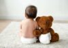 Baby in diaper sitting with teddy bear