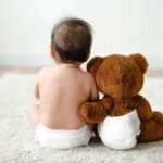 Baby in diaper sitting with teddy bear