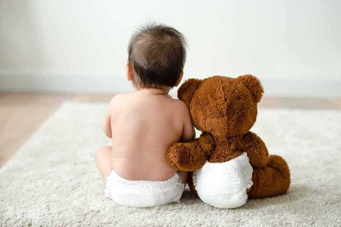 Baby in diaper sitting with teddy bear