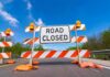 Powerless And Trapped – Jersey Floods Surge Road closed barricade with orange sandbags on a sunny day