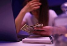 Person counting cash beside a laptop