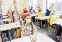 students wearing masks raise hands in a classroom