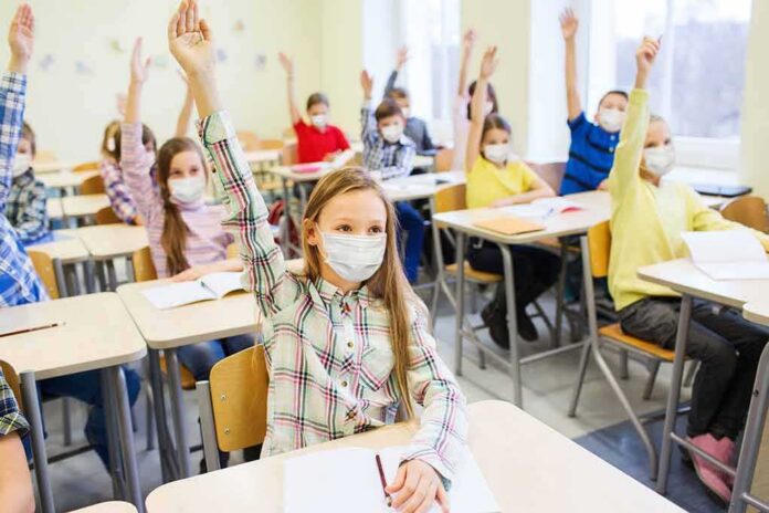 students wearing masks raise hands in a classroom