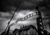 Entrance gate with wrought-iron sign at a historic brick complex under stormy skies