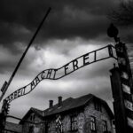 Entrance gate with wrought-iron sign at a historic brick complex under stormy skies
