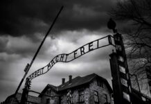 Entrance gate with wrought-iron sign at a historic brick complex under stormy skies