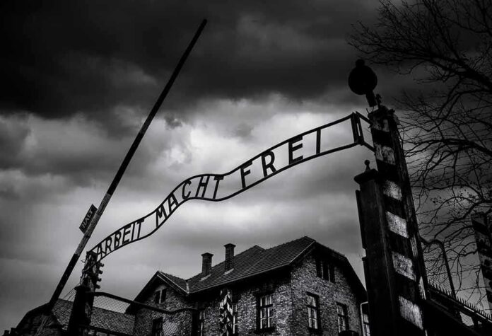shutterstock_1813188355 Entrance gate with wrought-iron sign at a historic brick complex under stormy skies