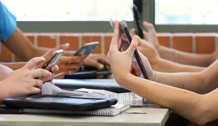 shutterstock_1847575498 students' hands using smartphones at a classroom table