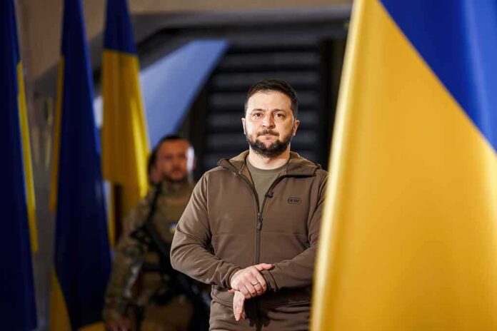 man in olive jacket standing between large blue and yellow flags