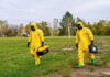 Biohazard Scare Freezes Oceanside Streets Two people in yellow hazmat suits walking across a grassy field