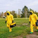 Two people in yellow hazmat suits walking across a grassy field