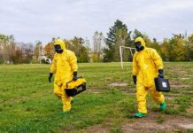 Biohazard Scare Freezes Oceanside Streets Two people in yellow hazmat suits walking across a grassy field
