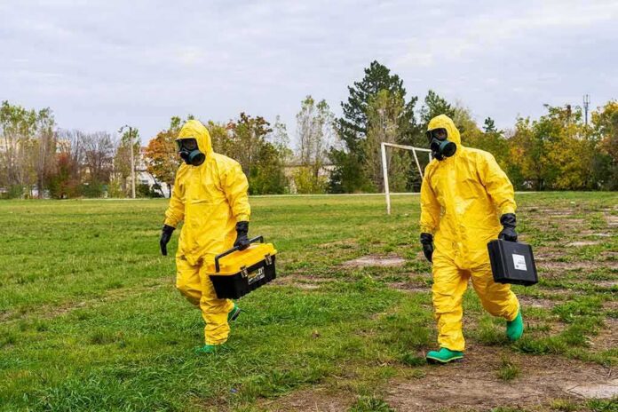 shutterstock_2226094877 Two people in yellow hazmat suits walking across a grassy field