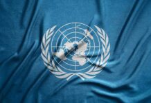 U.S.-Backed Block – UN Travel Ban Slams Iran’s Nuclear Boss United Nations flag featuring a world map and olive branches on a blue background
