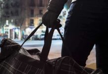 Person with gloved hand holding a duffel bag on a city street