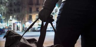 Person with gloved hand holding a duffel bag on a city street