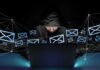 Hooded person using a laptop surrounded by email icons