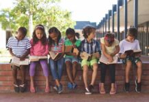 children sitting on a brick ledge reading books