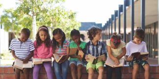 children sitting on a brick ledge reading books